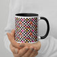 A person holds a vibrant My Favourite Colour is Rainbow Galaxy Mug featuring checkered patterns, stars, rainbows, and smiling faces on white ceramic. Its sleek black handle stands out against the persons light-colored sweater.