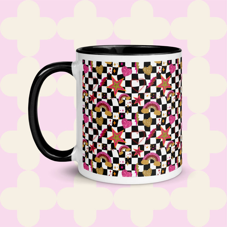 The Galaxy Mug by My Favourite Colour is Rainbow is a ceramic masterpiece featuring a black handle and rim, vibrant stars, hearts, rainbows, and squares on a light pink backdrop with white quatrefoil patterns.