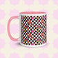 The Galaxy Mug from My Favourite Colour is Rainbow features a vibrant design with stars, hearts, rainbows, and checkerboard patterns in pink, gold, and black. It has a pink ceramic interior and handle with a charming pink and white geometric pattern background.