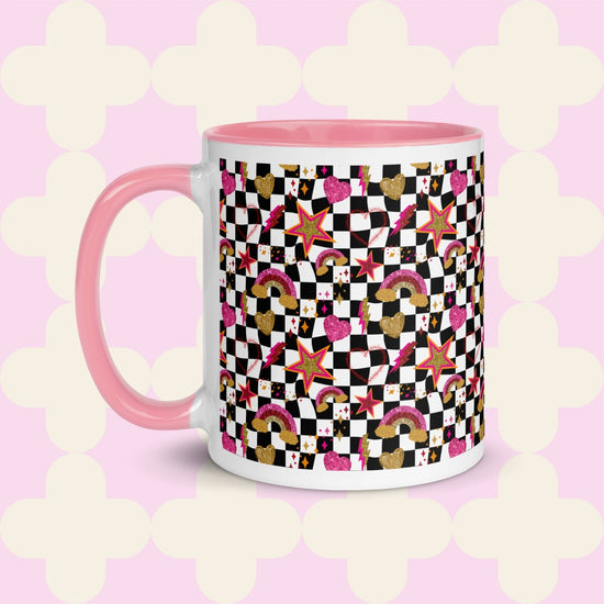 The Galaxy Mug from My Favourite Colour is Rainbow features a vibrant design with stars, hearts, rainbows, and checkerboard patterns in pink, gold, and black. It has a pink ceramic interior and handle with a charming pink and white geometric pattern background.