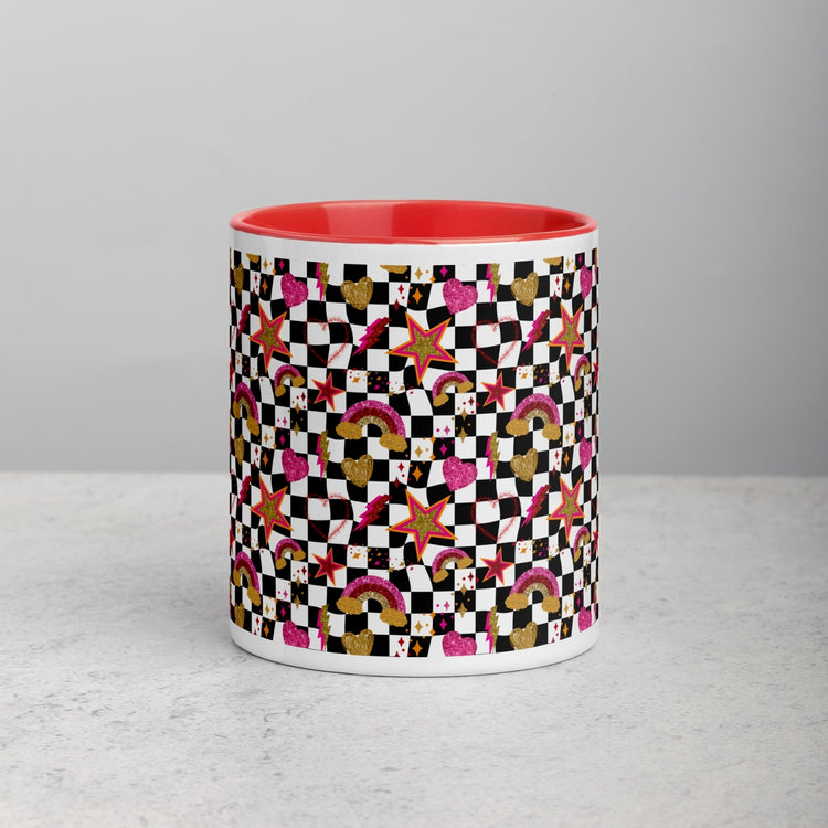 The Galaxy Mug by My Favourite Colour is Rainbow is a ceramic cylinder with a checkered design featuring stars, hearts, rainbows, and various shapes in black, white, pink, green, and yellow on a red interior. This colorful mug sits elegantly on a light gray surface.