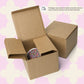 Two open brown cardboard boxes sit on a light pink patterned background. One contains a checkered roll, while the closed box hints at variety and protection, possibly holding My Favourite Colour is Rainbows vibrant Galaxy Mug or a delicate ceramic treasure.