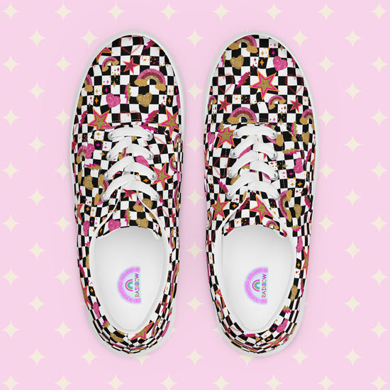 The Galaxy Canvas Sneakers by My Favourite Colour is Rainbow are decorated with a black and white checkerboard pattern, featuring gold, pink and red stars, hearts and rainbows. The inside of the shoes are white with My Favourite Colour is Rainbow branding on the footbed.  The shoes are shown on a pink background.  