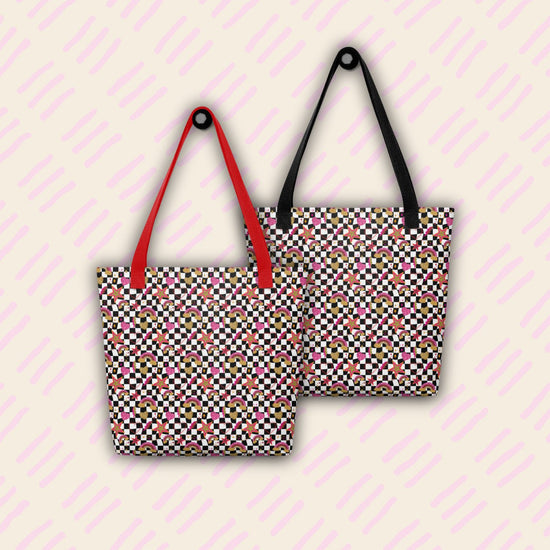 Two Galaxy Tote Bags by My Favourite Colour is Rainbow hang on hooks against a pale background, one with red handles and one with black.  The bags are decorated with a black-and-white checkerboard pattern with stars, rainbows and hearts in glittery gold, pink and red.