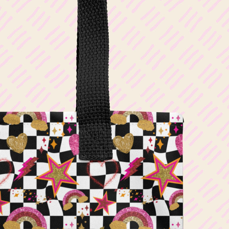 Close-up of the Galaxy Tote Bag by My Favourite Colour is Rainbow, featuring a black handle and a checkered pattern with colourful stars, rainbows, lightning bolts, hearts, and clouds in gold, pink, and red.