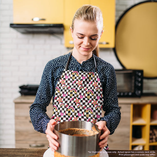 In a vibrant kitchen with yellow cabinets and a microwave, a blonde woman wears the Galaxy Apron by My Favourite Colour is Rainbow. She looks down at the crumbly crust inside her round baking pan.