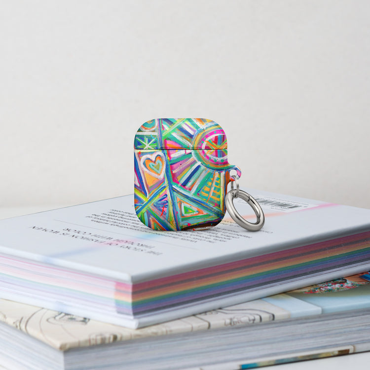 The Geometric Rainbow Airpods Gen 1 Case stands on a stack of books.  It features  an abstract design of colourful green, pink, yellow, blue, and purple stripes, dots, and zigzags.
