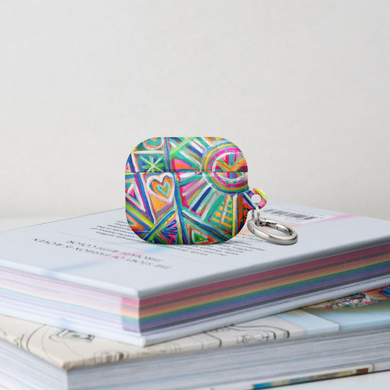 The Geometric Rainbow Airpods Gen 3 Case stands on a stack of books.  It features  an abstract design of colourful green, pink, yellow, blue, and purple stripes, dots, and zigzags. 
