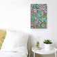 A vibrant 12x18 Geometric Rainbow canvas artwork by My Favourite Colour is Rainbow is mounted on a white wall. Below, a white bed with a yellow pillow sits next to a small round table with a lightbulb lamp and potted plant.