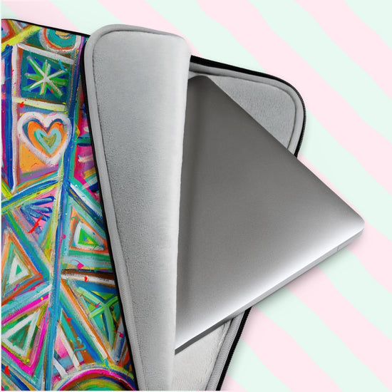 A silver laptop peeks out from the Geometric Rainbow Laptop Sleeve by My Favourite Colour is Rainbow, featuring a colorful abstract pattern with a zippered opening. This scratch-proof, splash-resistant sleeve rests against pink and green diagonal stripes.