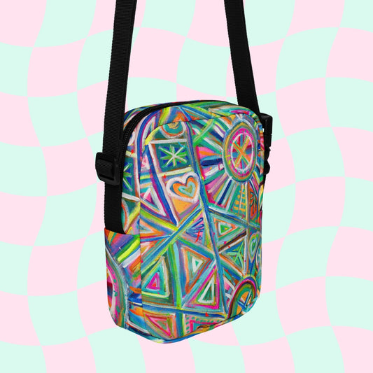 The Geometric Rainbow Mini Crossbody Bag by My Favourite Colour is Rainbow features a geometric rainbow print with hearts and stars, vibrant pink, green, blue, and orange shades, adjustable straps for versatile styling, and hangs against a pastel checkered background.