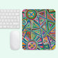 The Geometric Rainbow Mouse Pad by My Favourite Colour is Rainbow showcases vibrant patterns of triangles, circles, and hearts in green, red, blue, orange, and pink. A white keyboard and mouse are placed on the left side.