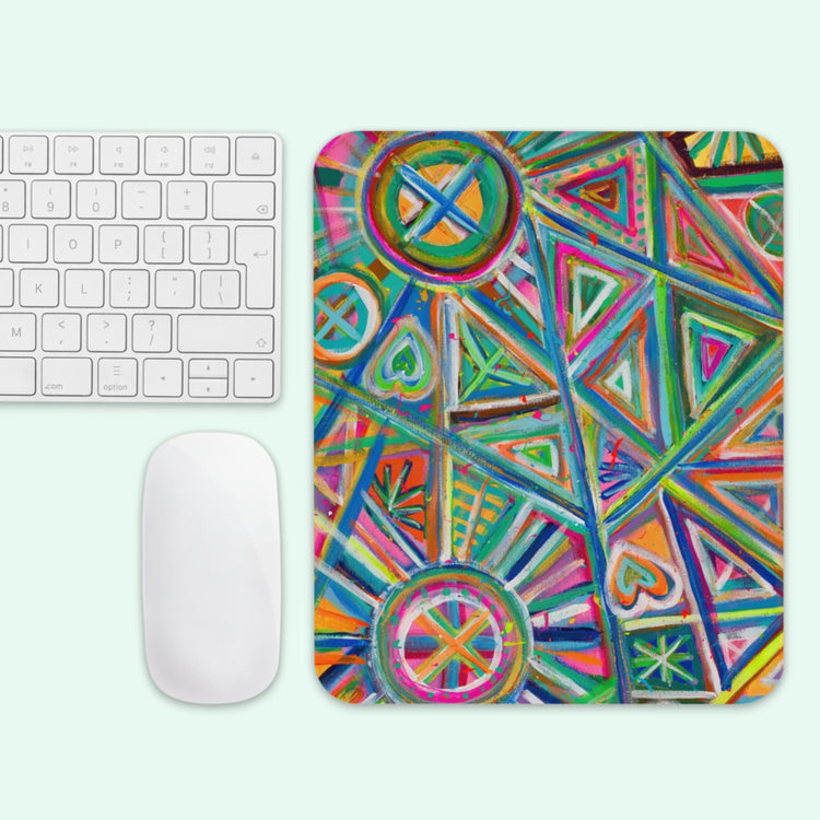 The Geometric Rainbow Mouse Pad by My Favourite Colour is Rainbow showcases vibrant patterns of triangles, circles, and hearts in green, red, blue, orange, and pink. A white keyboard and mouse are placed on the left side.