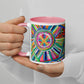 A person in a white sweater holds the Geometric Rainbow Mug by My Favourite Colour is Rainbow, featuring a pink interior and handle with abstract colorful circular and linear patterns, set against a plain background.