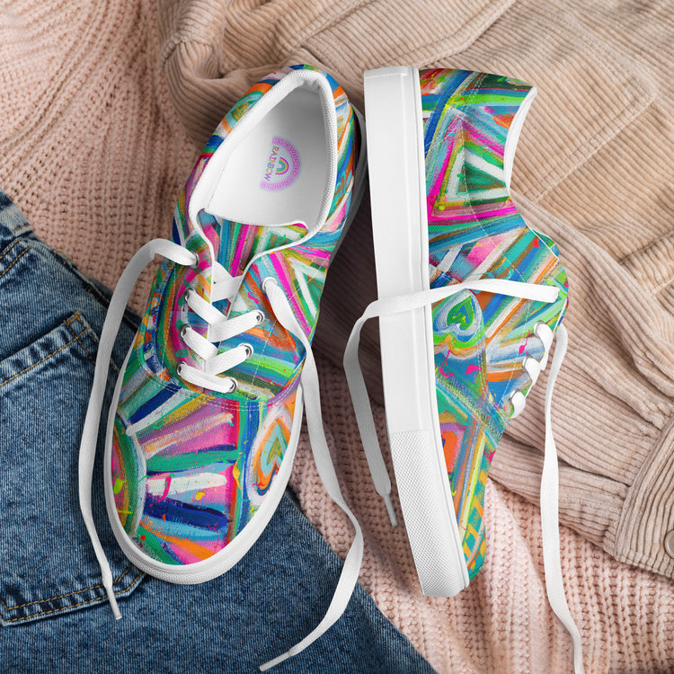 My Favourite Colour is Rainbows Geometric Rainbow Canvas Sneakers feature abstract geometric patterns in green, blue, pink, and orange on canvas with white laces and soles. They rest on textured beige fabric with denim nearby.