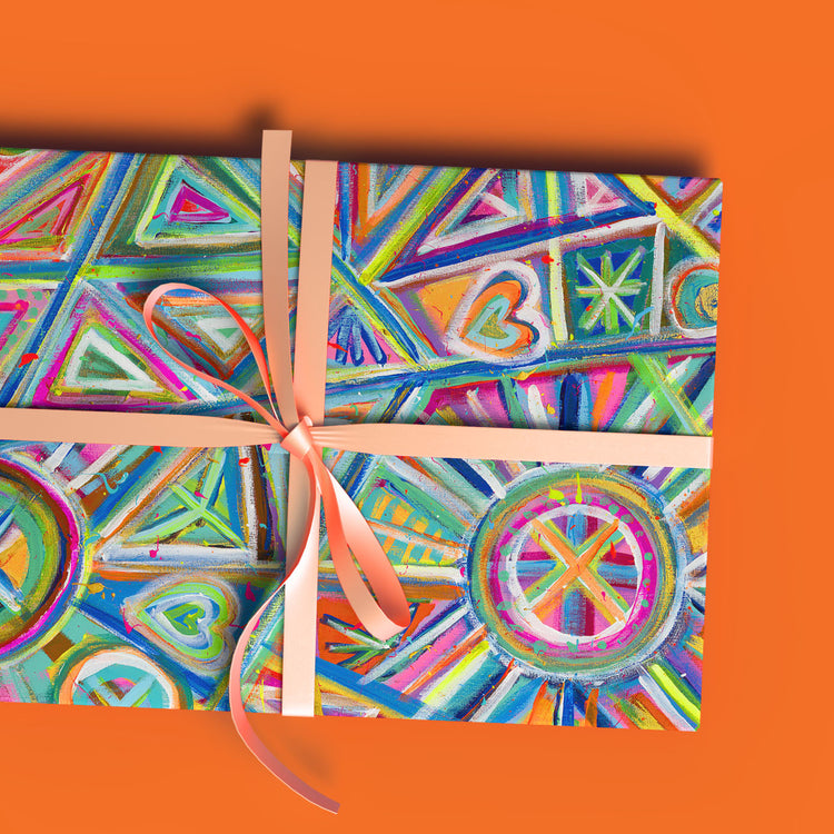 A colorful gift is wrapped in Geometric Rainbow Wrapping Paper Sheets by My Favourite Colour is Rainbow, featuring vibrant geometric shapes and patterns, secured with a peach ribbon and bow against a bright orange background.