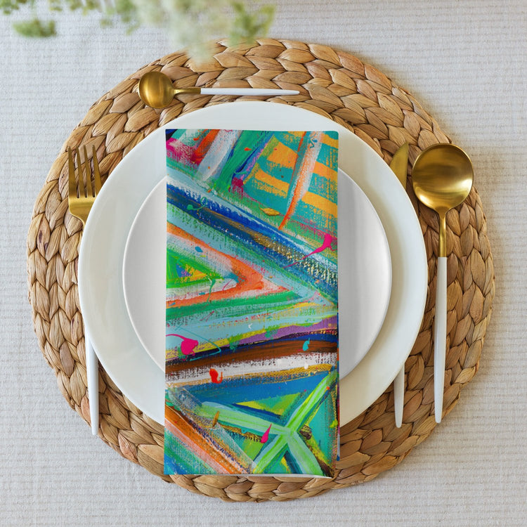 A Geometric Rainbow Cloth Napkin from My Favourite Colour is Rainbow graces a white plate. Paired with gold cutlery and set on a woven placemat over a white tablecloth, it transforms the dining experience into an elegant affair.