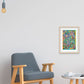 A minimalist interior features a wooden armchair with gray upholstery and a small round table. A colorful Geometric Rainbow Fine Art Print by My Store adorns the white wall beneath a bare bulb light. A cup sits on the table atop the wooden floor, adding elegance to the serene space.