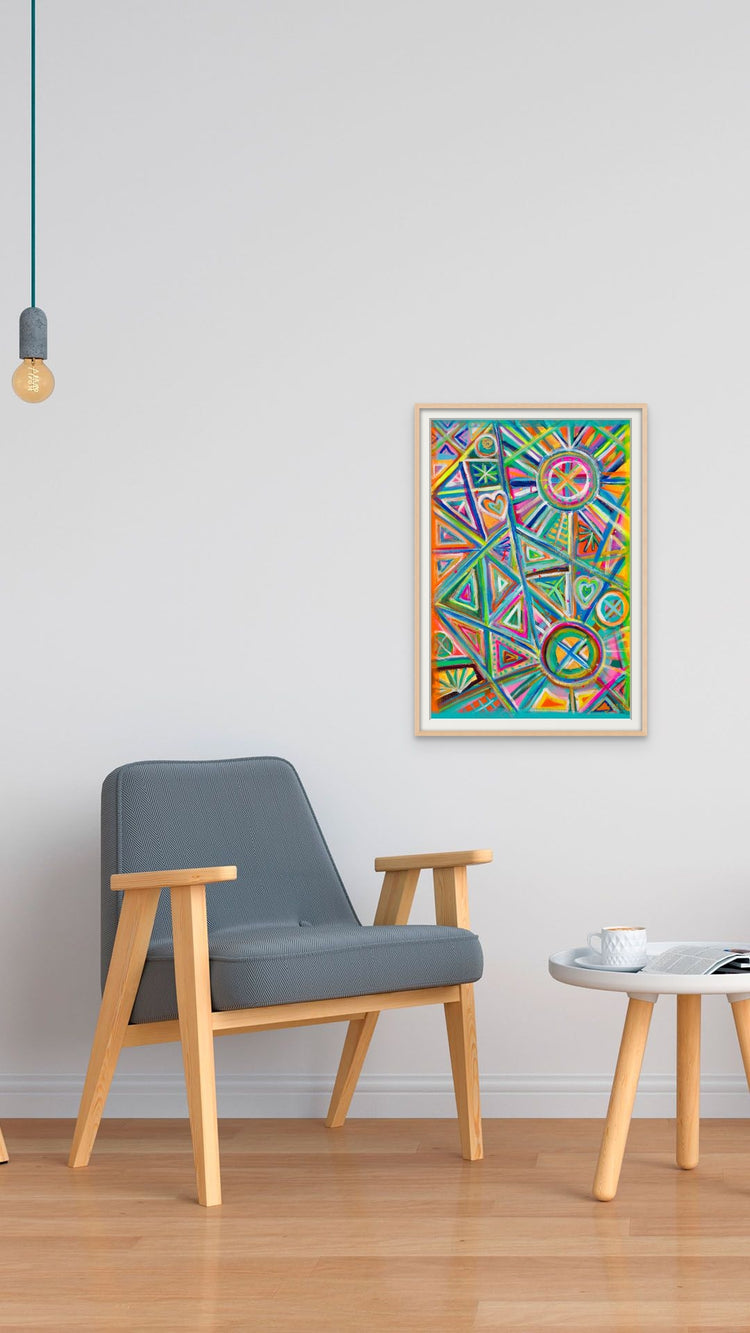 A minimalist room features a gray armchair and a wooden table on a wood floor. The Geometric Rainbow Fine Art Print by My Store hangs on the white wall in a wooden frame. A pendant light bulb hangs above, and a cup and saucer rest on the table.