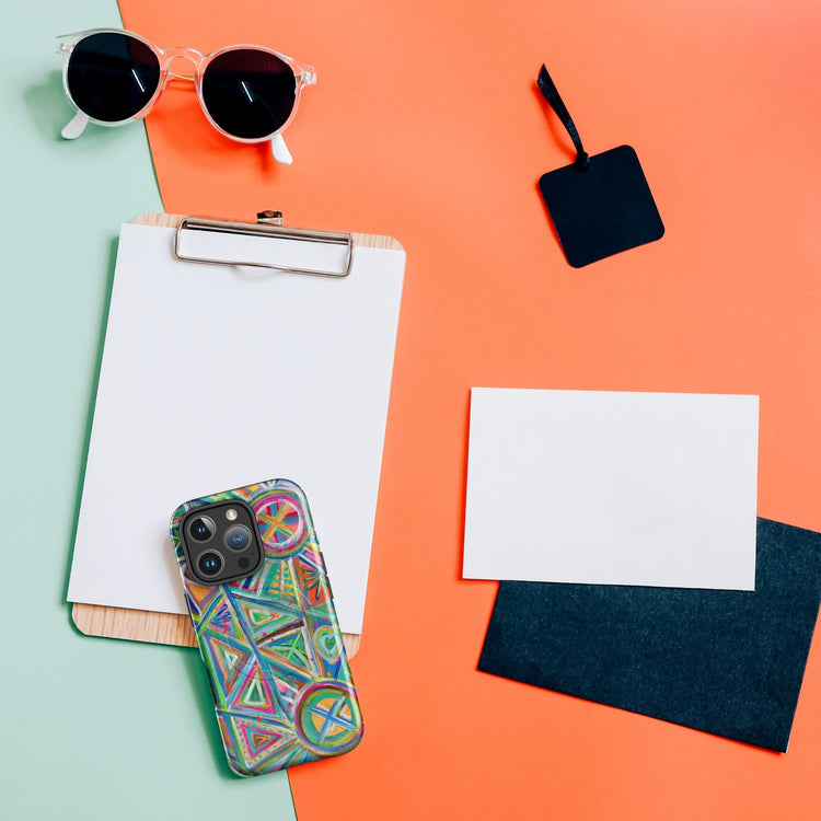 A flat lay on a pastel green and orange background includes sunglasses, a clipboard with blank paper, three blank cards in black, white, and dark blue, and a Geometric Rainbow MagSafe® iPhone Case by My Favourite Colour is Rainbow that adds vibrancy to the scene.