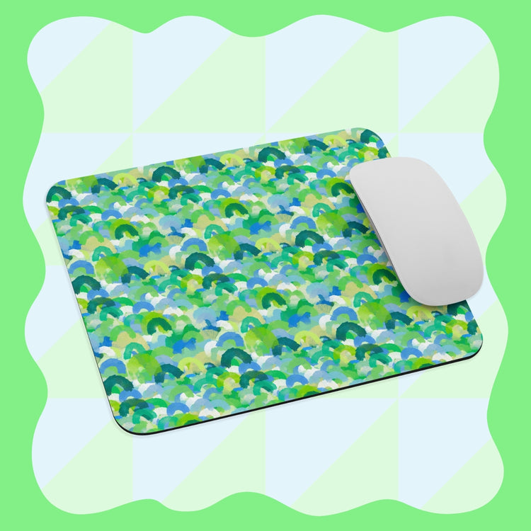 A sleek white computer mouse rests on a Green Rainbow Mouse Pad by My Favourite Colour is Rainbow, featuring an abstract green, blue, and white pattern. The light green background has wavy borders.