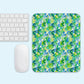 A white keyboard and mouse sit beside the Green Rainbow Mouse Pad by My Favourite Colour is Rainbow, featuring a vibrant abstract pattern in green, blue, and yellow on a light blue background.