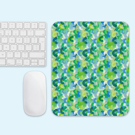 A white keyboard and mouse sit beside the Green Rainbow Mouse Pad by My Favourite Colour is Rainbow, featuring a vibrant abstract pattern in green, blue, and yellow on a light blue background.