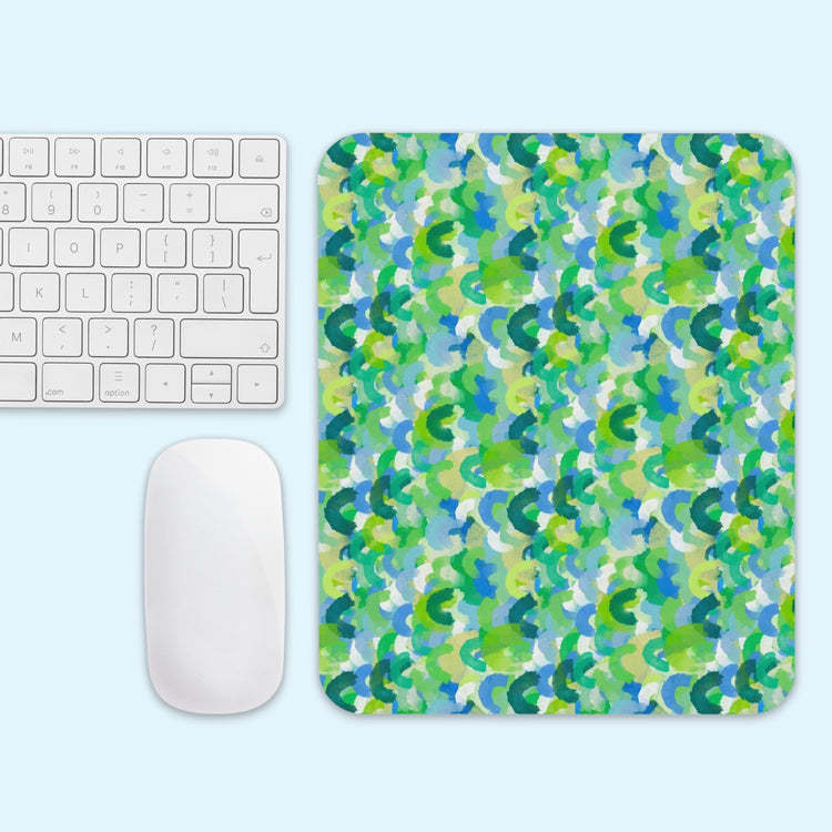 A white keyboard and mouse sit beside the Green Rainbow Mouse Pad by My Favourite Colour is Rainbow, featuring a vibrant abstract pattern in green, blue, and yellow on a light blue background.