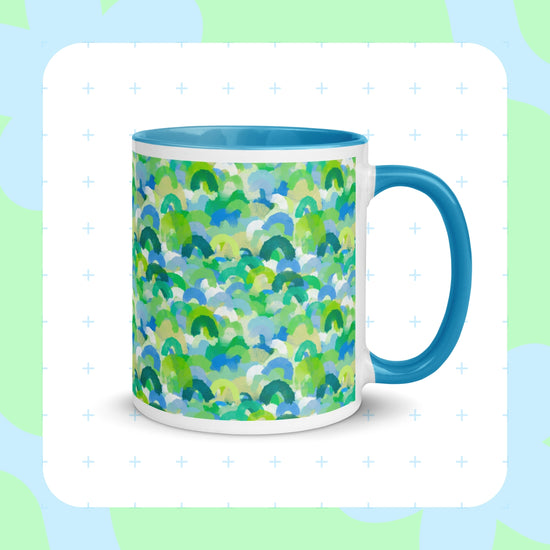 Introducing My Favourite Colour is Rainbows Green Rainbow Mug—a ceramic piece with green, blue, and white semi-circles like watercolor rainbows. It features a solid blue interior and handle, with a soft green and blue background accented by a delicate plus-sign pattern.