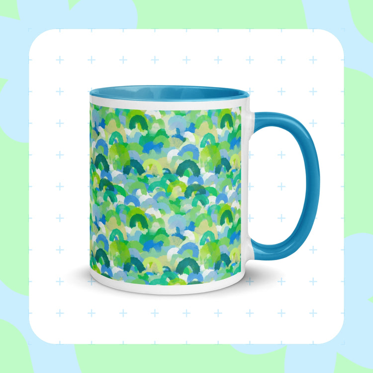 Introducing My Favourite Colour is Rainbows Green Rainbow Mug—a ceramic piece with green, blue, and white semi-circles like watercolor rainbows. It features a solid blue interior and handle, with a soft green and blue background accented by a delicate plus-sign pattern.