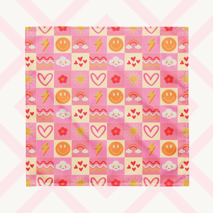 The Happy Smiles Sunny Days Bandana by My Favourite Colour is Rainbow features a vibrant pattern of smiley faces, lightning bolts, hearts, clouds, flowers, and waves on a pink and cream checkered background. 