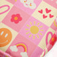 The Happy Smiles Sunny Days Mini Crossbody Bag by My Favourite Colour is Rainbow showcases a pink checkered fabric with cheerful designs—smiling faces, clouds, hearts, flowers, sun, and rainbows. Vibrant colours include pink accented by yellow, red, orange, and white. Adjustable straps add convenience.