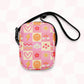 The Happy Smiles Sunny Days Mini Crossbody Bag by My Favourite Colour is Rainbow is a sturdy canvas bag decorated with bright icons like smiley faces, hearts, and more atop a pink checkered background.  It has internal and external pockets and a black strap with a clip on one side that can be extended to crossbody length.