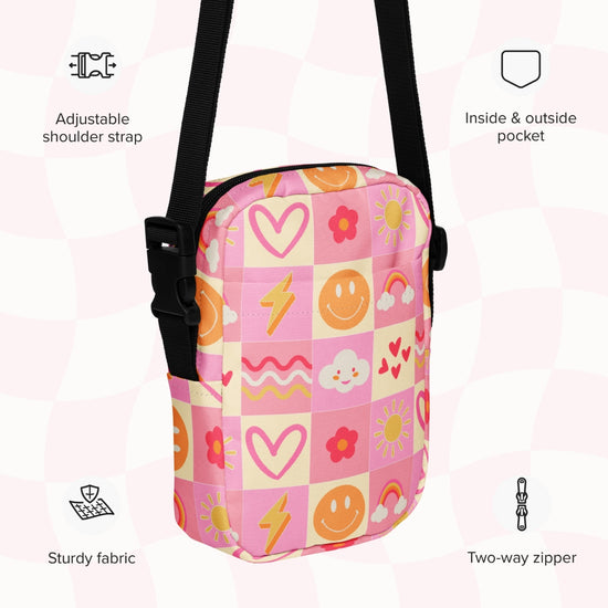 The Happy Smiles Sunny Days Mini Crossbody Bag by My Favourite Colour is Rainbow is a sturdy, durable fabric bag in a pink, orange, and yellow checkered pattern with hearts, smileys, and flowers. It features an adjustable shoulder strap, two-way zipper, plus inside and outside pockets for adventures.