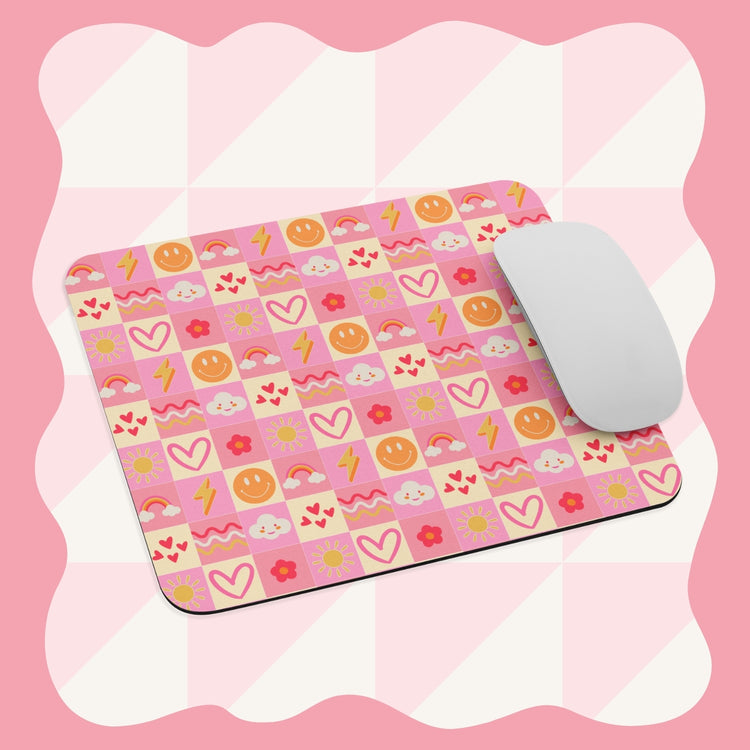 The Happy Smiles Sunny Days Mouse Pad by My Favourite Colour is Rainbow features a vibrant pink and white checkerboard pattern with hearts, smiley faces, suns, clouds, rainbows, lightning bolts, and flowers. A white computer mouse rests on the pad.