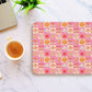 A laptop and coffee rest on marble beside the Happy Smiles Sunny Days Mouse Pad by My Favourite Colour is Rainbow, featuring smiley faces, clouds, suns, lightnings, flowers, and rainbows. A small plant peeks into view above.