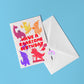 The Have a Roarsome Birthday Card by My Store features fun cartoon dinosaurs and red text on a light blue surface, paired with a white envelope and rainbow sticker.