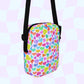 The Heart Attack Mini Crossbody Bag by My Favourite Colour is Rainbow features a multicolored heart print in blue, purple, orange, pink, red, and green on a light checkered background. It has black adjustable straps and offers vibrant style.