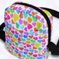 The Heart Attack Mini Crossbody Bag by My Favourite Colour is Rainbow features a lively print with colorful hearts on white, including bright red, blue, green, yellow, and purple shades. It has black adjustable straps and a top zipper for convenience.