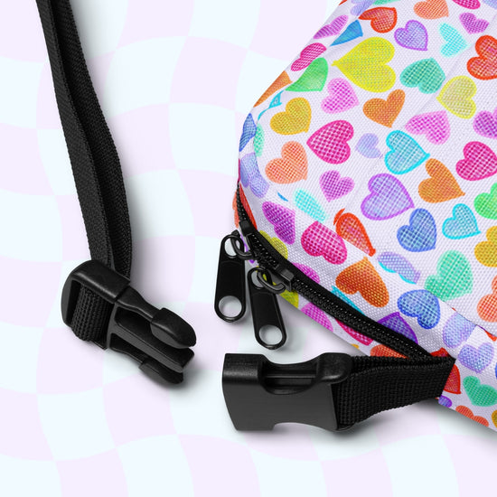 Close-up of the Heart Attack Mini Crossbody Bag by My Favourite Colour is Rainbow. It has a vibrant print, two black zippers, and an adjustable black strap against a subtly checkered white background.