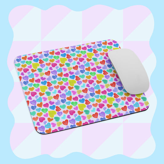 A mouse on the Heart Attack Mouse Pad by My Favourite Colour is Rainbow, featuring multicolored hearts on a light blue background with a subtle pink and white pattern.