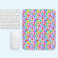 A mouse and keyboard are placed beside the Heart Attack Mouse Pad by My Favourite Colour is Rainbow, showcasing a vibrant pattern of red, blue, green, purple, and yellow hearts on a light blue background.