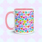 The Heart Attack Mug by My Favourite Colour is Rainbow features a pink interior and handle, with a vibrant pattern of overlapping hearts in bright blue, purple, yellow, and pink on a pastel background.