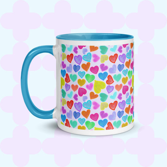 The Heart Attack Mug by My Favourite Colour is Rainbow showcases a vibrant heart pattern in pink, purple, blue, green, and yellow on a white background, complemented by a blue handle and interior.