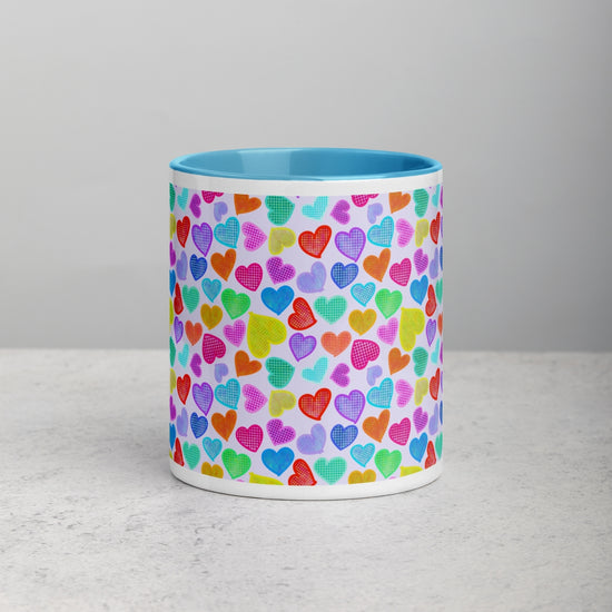 Front view of the Heart Attack Mug by My Favourite Colour is Rainbow, featuring a vibrant heart pattern in red, blue, green, purple, and orange.  It has a sky-blue interior and handle.