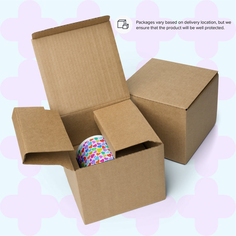 An open cardboard box with a Heart Attack Mug from My Favourite Colour is Rainbow shows the colourful rainbow heart pattern. A closed box sits beside it. Text indicates packaging varies by location but ensures product protection.