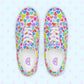 Introducing the My Favourite Colour is Rainbow's Heart Attack Canvas Sneakers, adorned with vibrant multicoloured hearts in red, blue, purple, and green. These sneakers feature white laces and soles.  The inside of the shoe is white with My Favourite Colour is Rainbow branding on the footbed.
