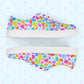 Side views of the Heart Attack Canvas Sneakers by My Favourite Colour is Rainbow, decorated with a colourful heart pattern on a light background. Displayed side by side, they showcase a vibrant, playful design and a comfy fit.