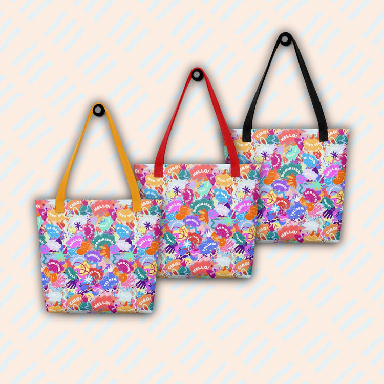 Three Hello! Wominjeka! Tote Bags by My Favourite Colour is Rainbow hang on a light patterned background, each with different handle colors (black, red, yellow), featuring spacious interiors and bold abstract design with "Hello" in various languages.