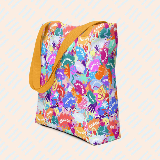 Hello! Wominjeka! Tote Bag by My Favourite Colour is Rainbow features bold abstract designs with "Hello" in various languages like hola and bonjour. It has a spacious design with a mustard yellow strap.